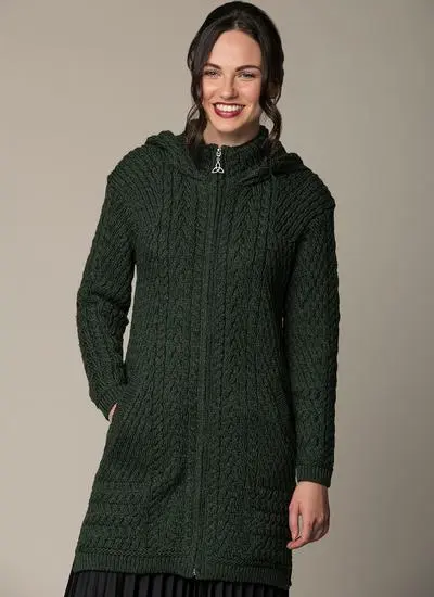 smiling brown haired woman wearing a dark green aran knitted coatigan with one hand in pocket